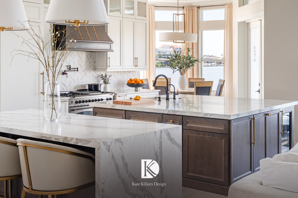 Custom kitchen with a marble waterfall island, dark wood cabinetry and brass hardware overlooking the water, by Kate Killeen Design