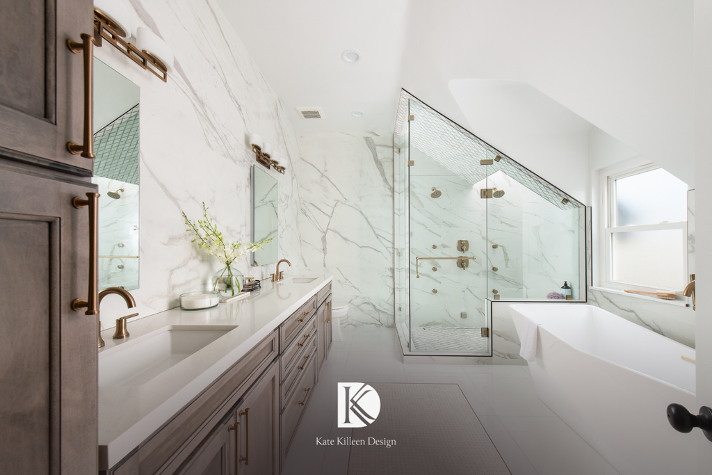 Primary bath in book-matched marble with a freestanding tub and vaulted glass shower, designed by Kate Killeen Design, a boutique interior designer
